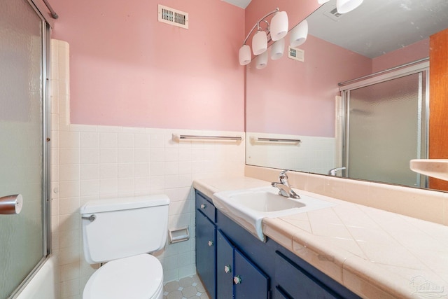 full bathroom featuring shower / bath combination with glass door, vanity, tile walls, and toilet