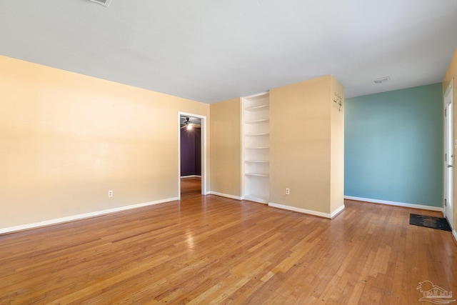 empty room featuring built in shelves and light hardwood / wood-style floors