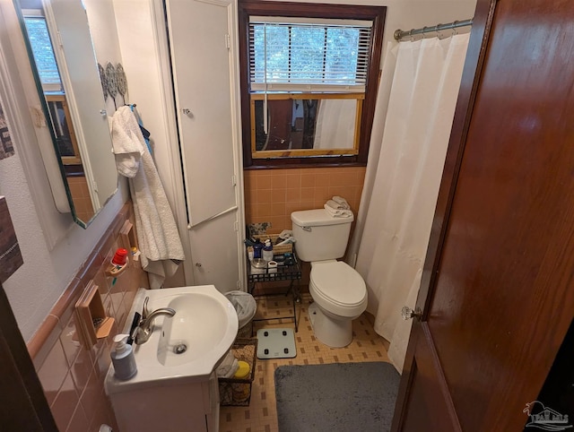 bathroom featuring a shower with shower curtain, tile walls, toilet, and a sink