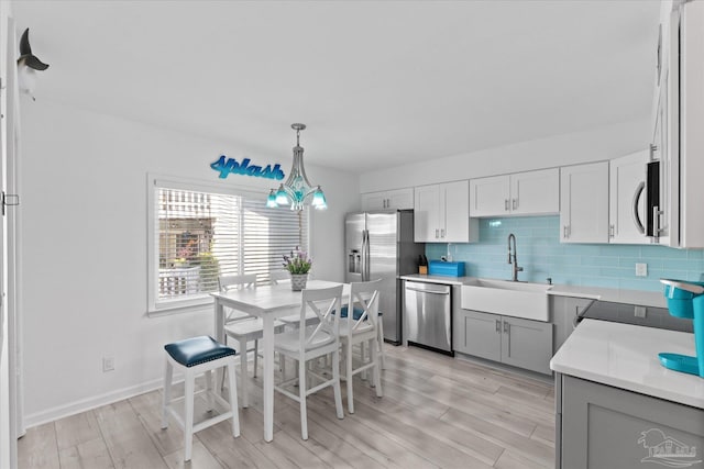 kitchen featuring backsplash, light hardwood / wood-style floors, pendant lighting, sink, and appliances with stainless steel finishes