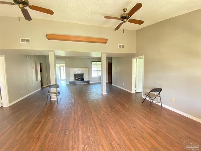 unfurnished living room with a high ceiling, ceiling fan, dark wood-type flooring, and a textured ceiling