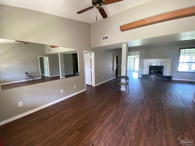 unfurnished living room with ceiling fan, a textured ceiling, dark wood-type flooring, and a high ceiling