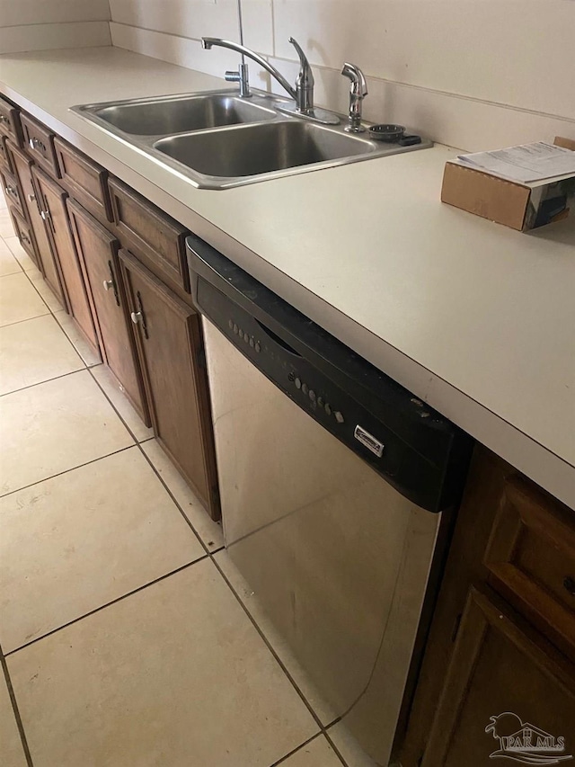 kitchen with dark brown cabinetry, sink, light tile patterned floors, and stainless steel dishwasher