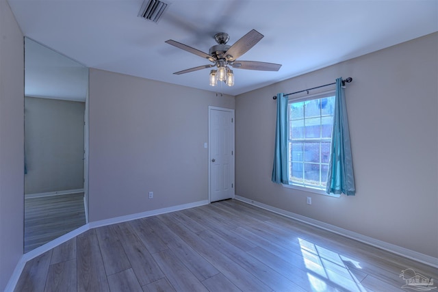 spare room featuring light wood-type flooring, baseboards, visible vents, and a ceiling fan