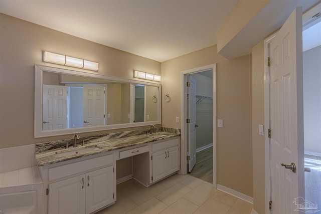 bathroom featuring a sink, a spacious closet, baseboards, and double vanity