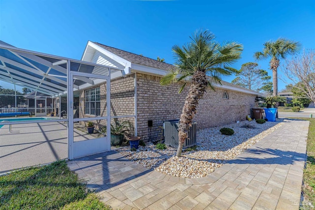 view of property exterior with a fenced in pool, brick siding, central air condition unit, a patio area, and a lanai