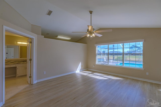 spare room featuring light wood finished floors, visible vents, a ceiling fan, vaulted ceiling, and baseboards