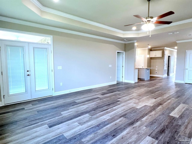 unfurnished living room with a tray ceiling, crown molding, dark hardwood / wood-style flooring, ceiling fan, and french doors