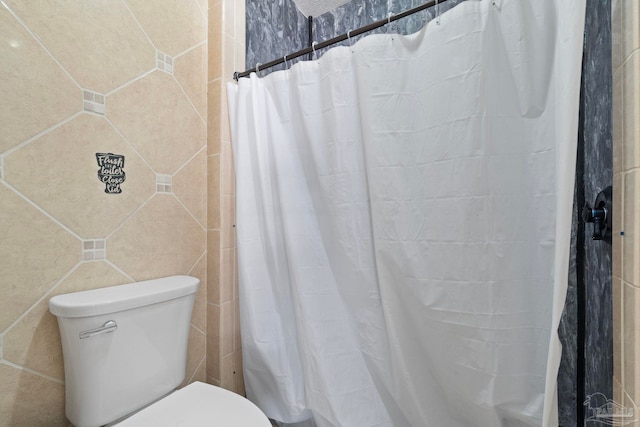 bathroom with toilet, curtained shower, and tile walls