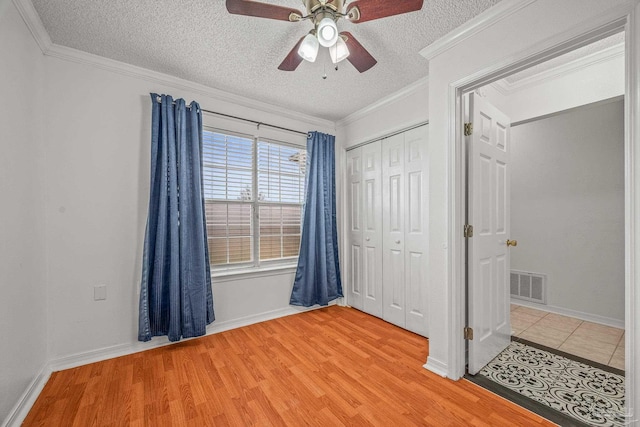 unfurnished bedroom with visible vents, crown molding, light wood-style floors, a closet, and a textured ceiling