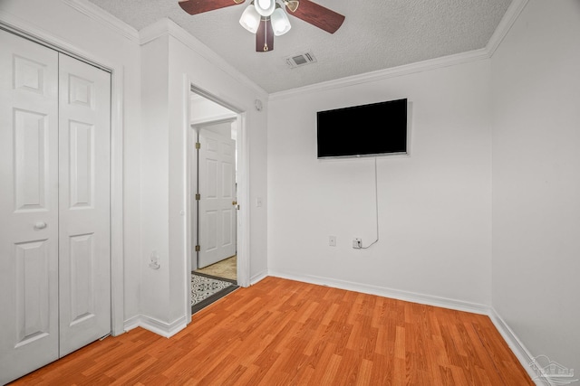 unfurnished bedroom featuring baseboards, visible vents, light wood-style flooring, ornamental molding, and a textured ceiling