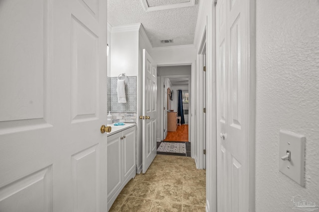 hall featuring visible vents, attic access, a textured ceiling, crown molding, and a textured wall