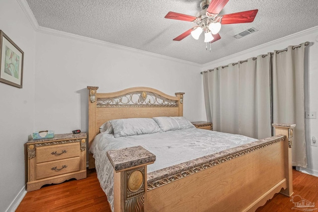 bedroom featuring a textured ceiling, wood finished floors, visible vents, and ornamental molding