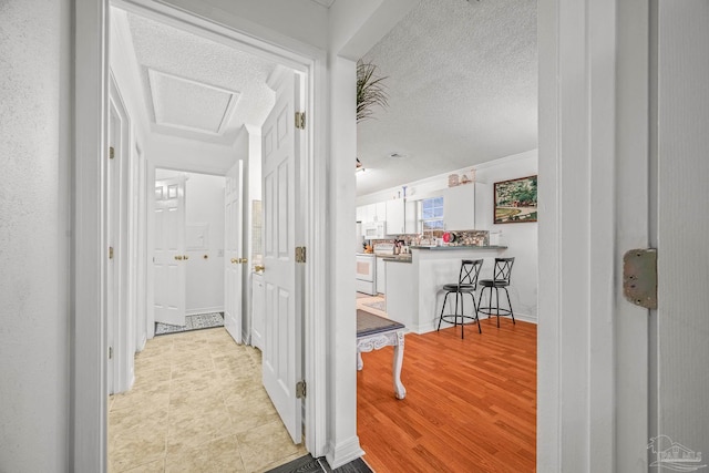 hallway featuring attic access, wood finished floors, and a textured ceiling