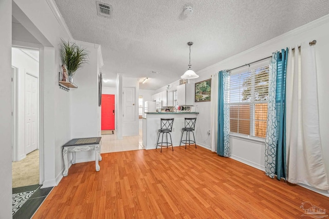 interior space featuring a textured ceiling, light wood-style floors, visible vents, and ornamental molding