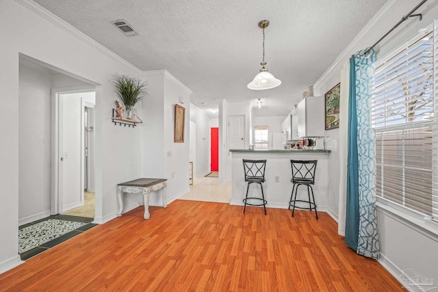 interior space featuring baseboards, visible vents, light wood-style flooring, a textured ceiling, and crown molding