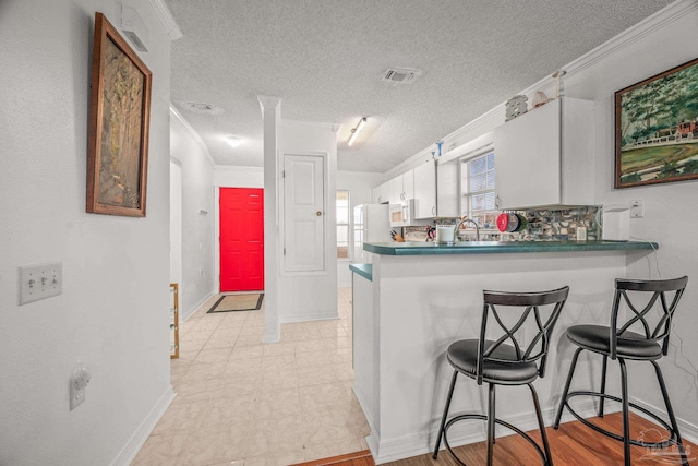 kitchen with visible vents, a breakfast bar area, ornamental molding, a peninsula, and white appliances