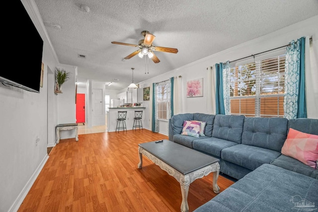 living area featuring ceiling fan, light wood-style floors, ornamental molding, and a textured ceiling