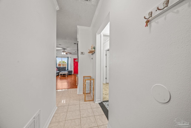 corridor with crown molding, light tile patterned floors, baseboards, and visible vents