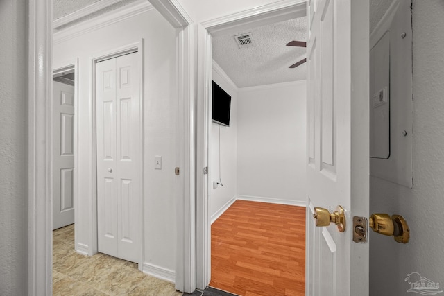 hallway featuring light wood finished floors, visible vents, crown molding, baseboards, and a textured ceiling