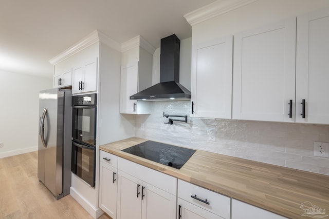 kitchen with white cabinets, backsplash, black appliances, wall chimney range hood, and light wood-type flooring