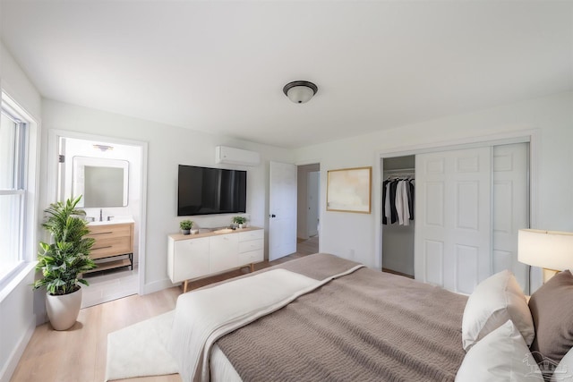 bedroom featuring connected bathroom, light hardwood / wood-style flooring, a wall mounted air conditioner, and a closet