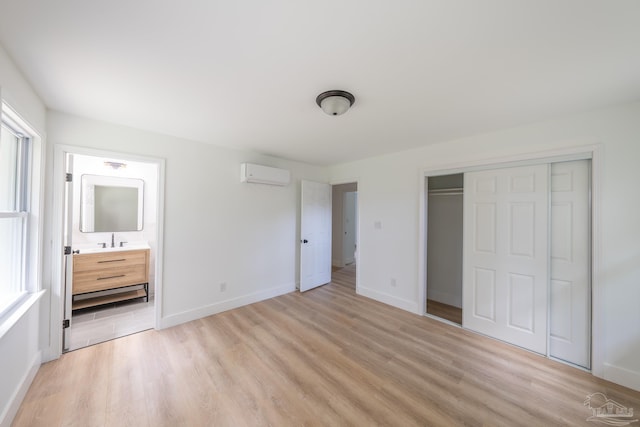 unfurnished bedroom featuring sink, ensuite bath, a wall mounted air conditioner, light hardwood / wood-style floors, and a closet