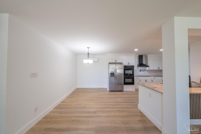 kitchen featuring wood counters, decorative light fixtures, stainless steel fridge, white cabinets, and wall chimney range hood