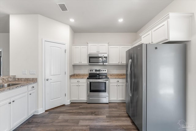 kitchen featuring appliances with stainless steel finishes, light stone counters, dark wood-type flooring, sink, and white cabinets