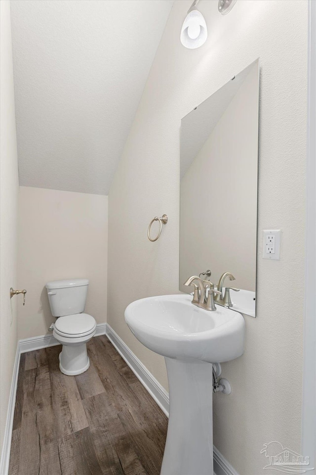 bathroom with wood-type flooring, vaulted ceiling, and toilet