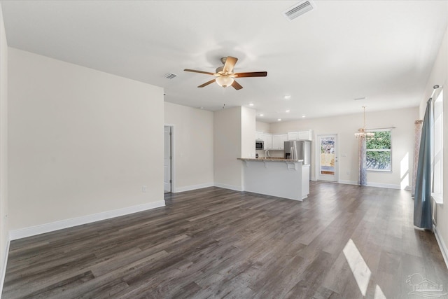 unfurnished living room featuring ceiling fan with notable chandelier and dark hardwood / wood-style flooring