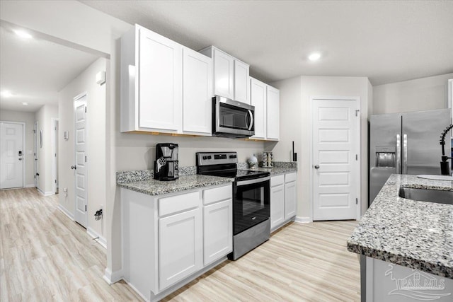 kitchen featuring baseboards, light wood-style floors, stainless steel appliances, and a sink