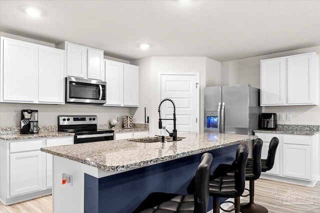 kitchen featuring a breakfast bar, a sink, stainless steel appliances, white cabinets, and light wood-type flooring