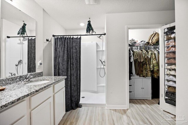 full bath featuring a shower stall, a spacious closet, vanity, and wood finished floors