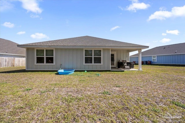 back of property with a patio, fence, board and batten siding, a yard, and roof with shingles