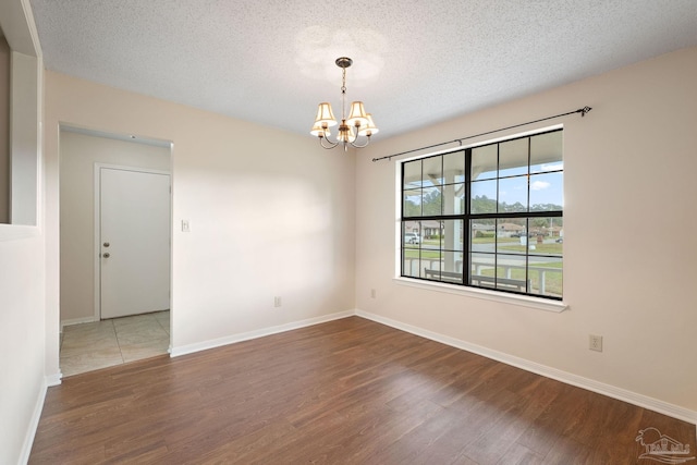 spare room featuring a notable chandelier, wood finished floors, and a textured ceiling