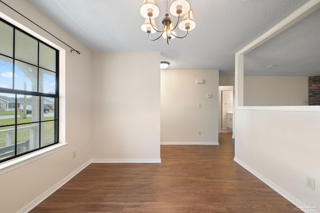 unfurnished room featuring a textured ceiling, wood finished floors, baseboards, and a chandelier