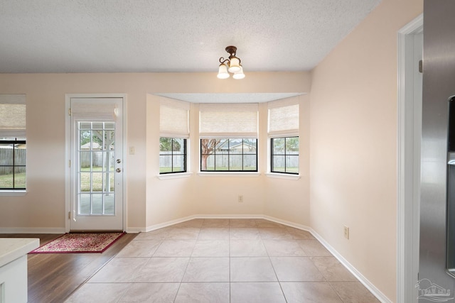 foyer entrance featuring light tile patterned flooring, a notable chandelier, a healthy amount of sunlight, and a textured ceiling