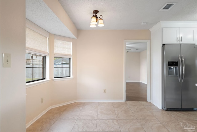 unfurnished dining area featuring light tile patterned floors, baseboards, visible vents, and a textured ceiling