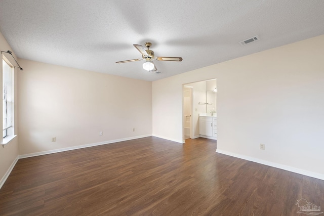 spare room with a ceiling fan, visible vents, baseboards, dark wood finished floors, and a textured ceiling