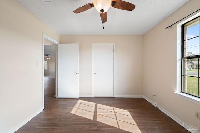 unfurnished bedroom featuring multiple windows, wood finished floors, baseboards, and a textured ceiling