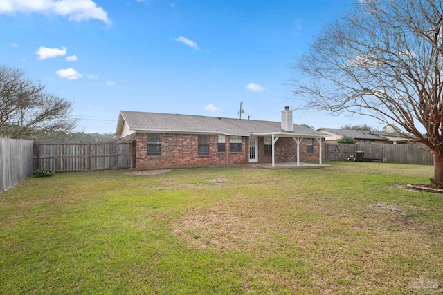 back of house with a fenced backyard, a yard, brick siding, a chimney, and a patio area