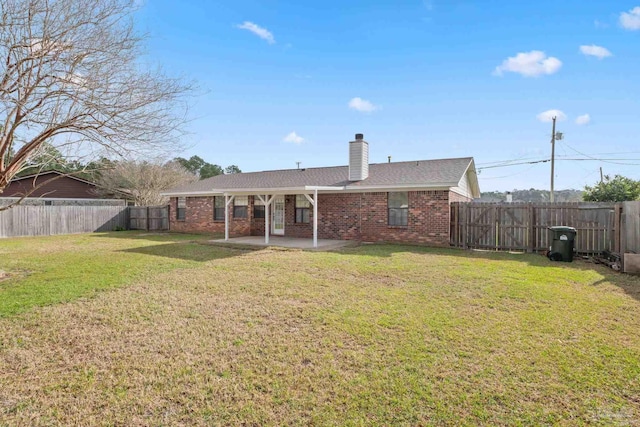 rear view of house with a patio, a fenced backyard, a yard, brick siding, and a chimney