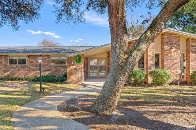 view of front of property with french doors, brick siding, and a front lawn