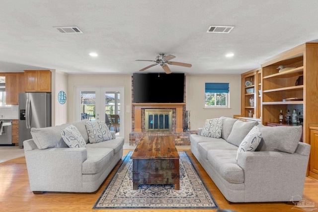 living area featuring light wood-style flooring, a fireplace, and visible vents