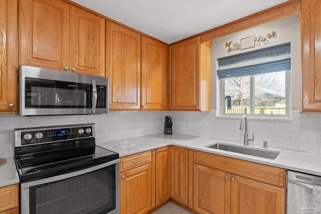 kitchen with light countertops, appliances with stainless steel finishes, a sink, and tasteful backsplash