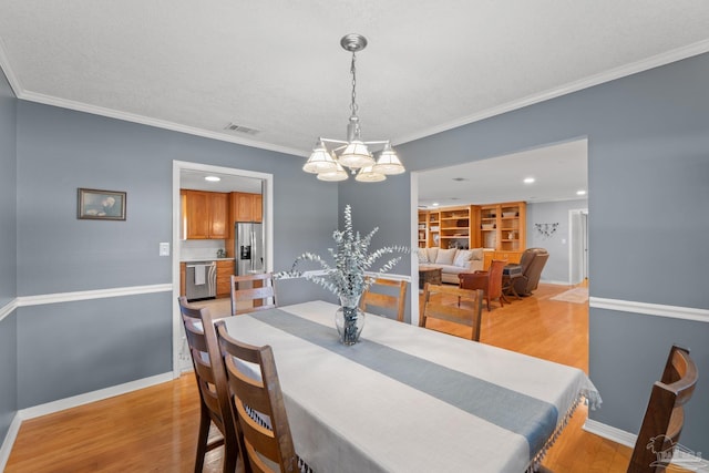 dining space with crown molding, visible vents, baseboards, light wood-type flooring, and an inviting chandelier