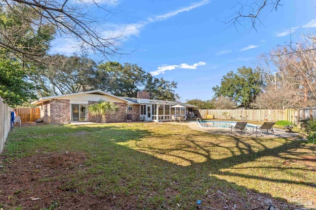 rear view of house with a fenced backyard, brick siding, a yard, a fenced in pool, and a chimney