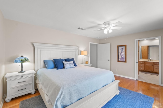 bedroom with ensuite bathroom, light wood finished floors, visible vents, and baseboards