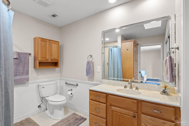 bathroom with toilet, vanity, visible vents, and wainscoting